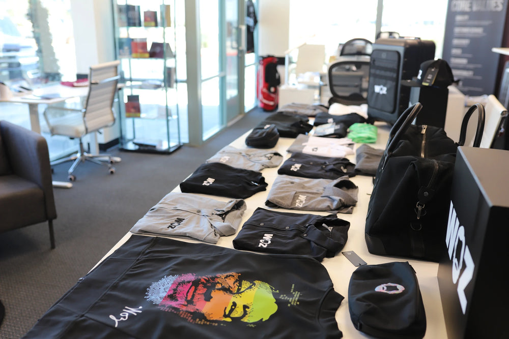 WOZ apparel, bags, caps, and luggage arranged on a showroom table.
