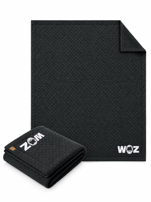 WOZ TravisMathew quilted blanket, shown folded and unfolded. One blanket included.