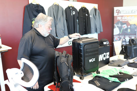 Woz resting a hand on black WOZ-branded wheeled luggage.