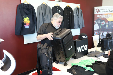 Woz tilting a black WOZ-branded suitcase to examine it.